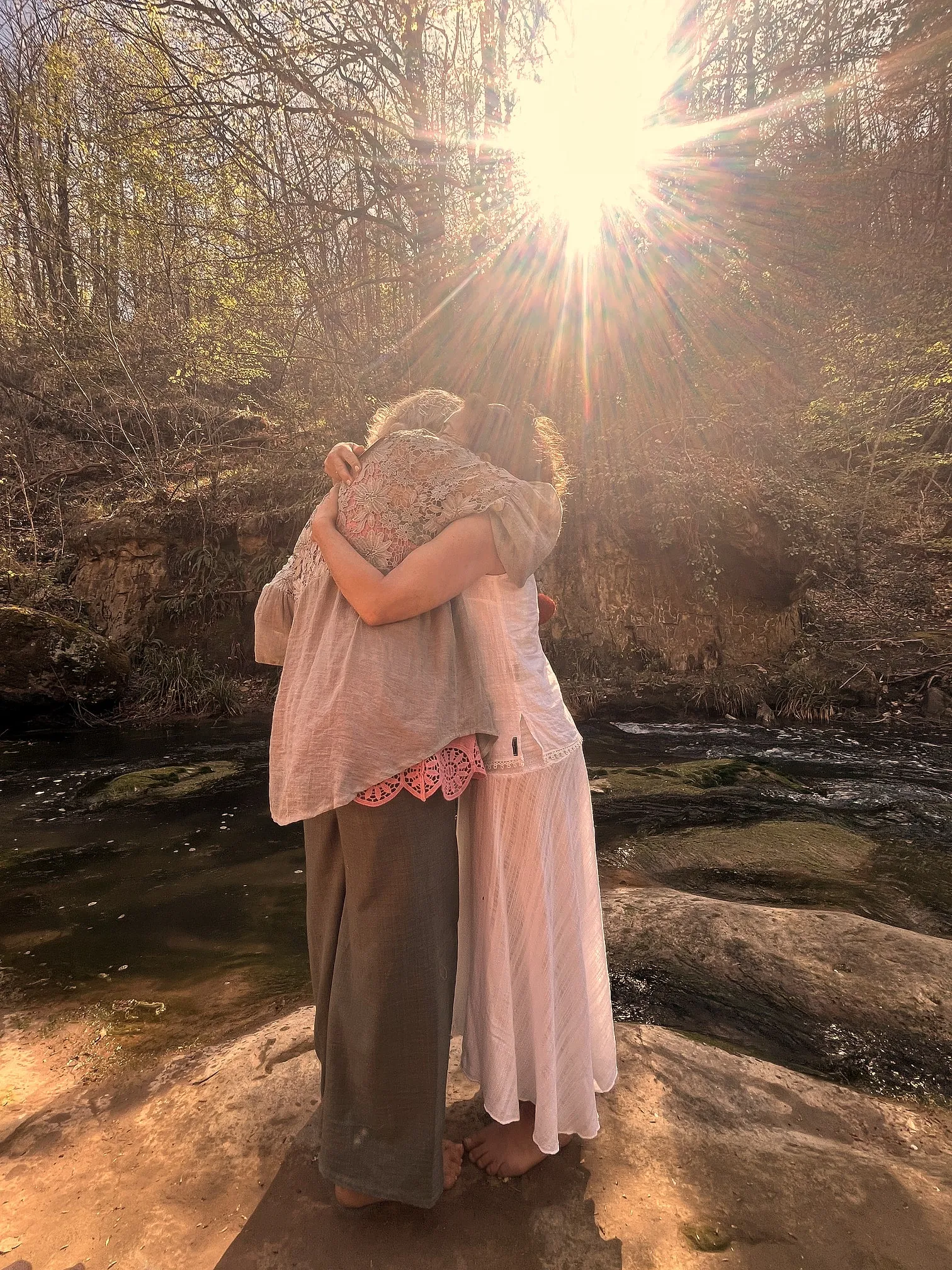 Zwei Frauen in einer innigen Umarmung am Bach, von Sonnenlicht durchflutet